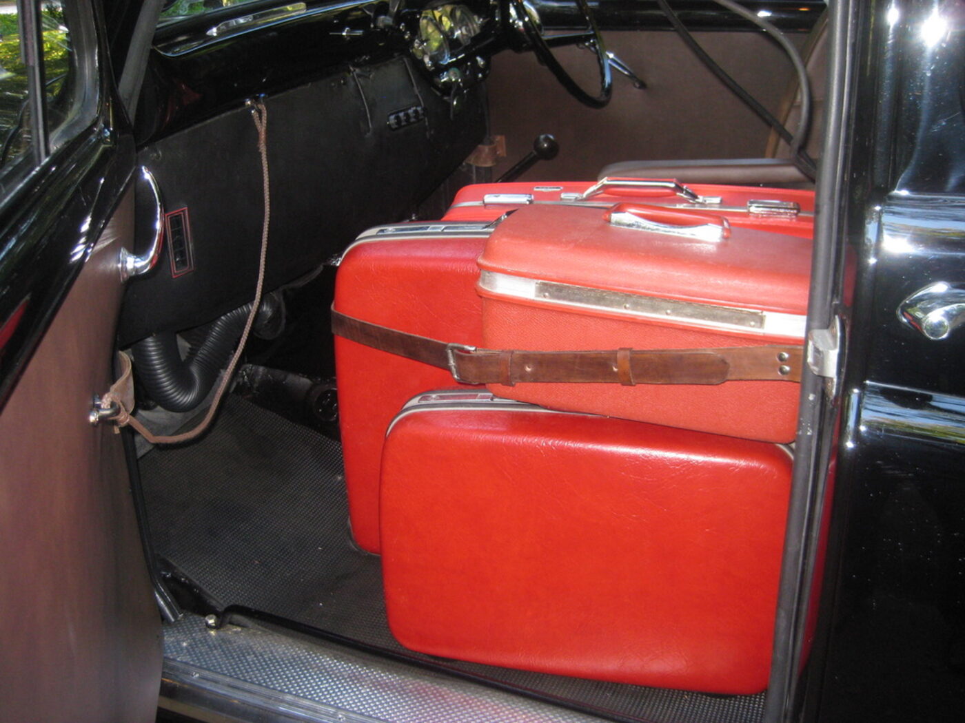 The open passenger compartment of the cab with two pieces of red vintage hand luggage strapped in place on the floor.
